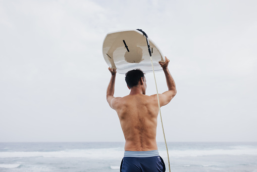 A determined surfer marching towards the waves, surfboard balanced on his head