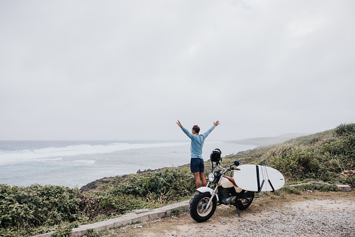 A rider with a surfboard on the side of his motorcycle, chasing the perfect surf spot along the scenic coastal route.
