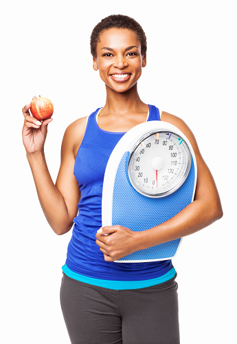 Portrait of a fit African American woman with weighing scale and a fresh apple. Vertical shot. Isolated on white.