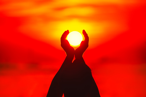 Silhouette of female hands holding the sun at sunset background