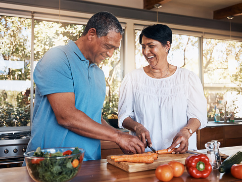 Mature, couple and healthy cooking in kitchen to chop vegetables for salad diet, nutrition and lunch meal at home. Happy man, woman and help cut carrot ingredients for love, care and support together