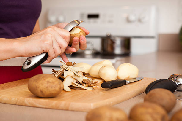 kolorowy obraz kobieta w jej kuchni obierka ziemniaki - potato skin zdjęcia i obrazy z banku zdjęć