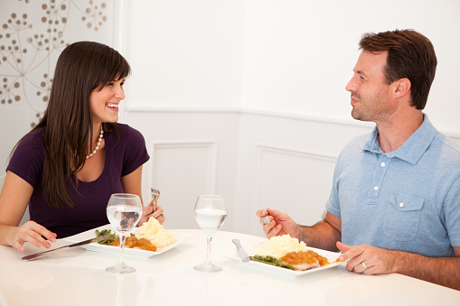Color image of a happy, young couple sitting together at the dining room table eating their dinner.