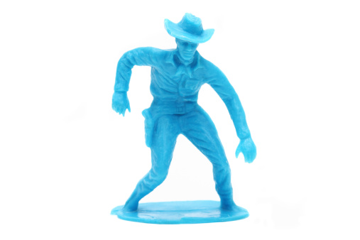A blue toy cowboy stands about to draw his pistol.  Studio shot on a white background. This is a generic toy cowboy without any marks or brand names.