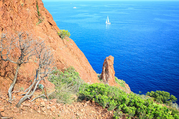 Sailboat in the Mediterrean at the peninsula Cap du Dramont near Frejus. The Cap du Dramont lies at the scenic coast road Corniche d'Or between Cannes and Frejus at the French Riviera below the Massif d'Esterel. It has the same red porphyry stones as the Massif d'Esterel.