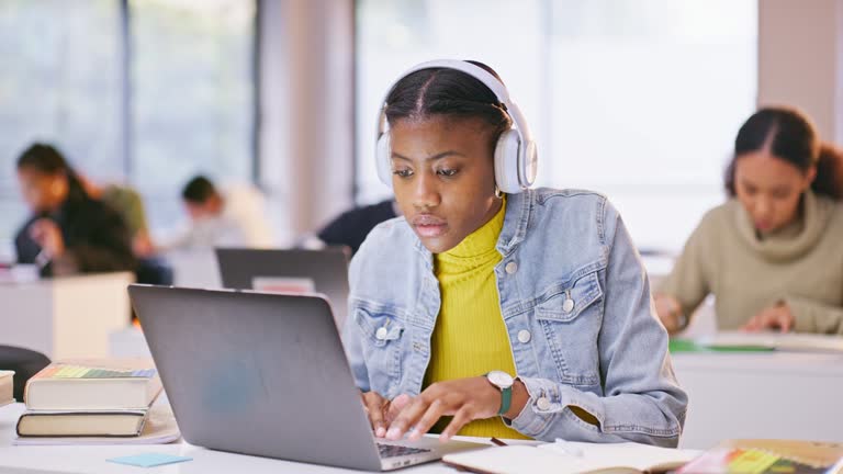 Headphones, laptop and black woman in the class listening to music, playlist or album at university. Technology, computer and female student working on assignment streaming song or radio in college.