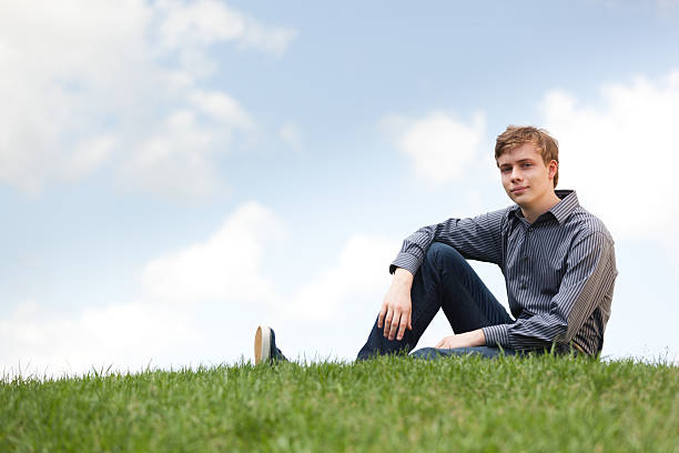 istock Young teenager man sitting on grass with sky background 175414327