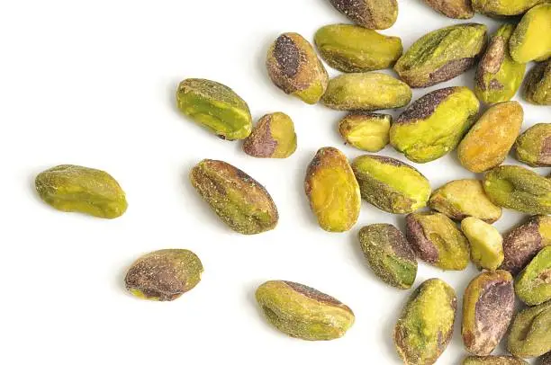 Shelled Pistachio nuts scattered across a white background.