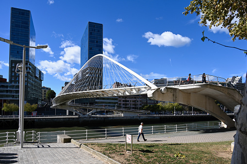 Bilbao, Spain, October 18, 2023 - The Zubizuri pedestrian bridge / Calatrava bridge designed by Spanish architect Santiago Calatrava and the Isozaki Atea twin towers in Bilbao.