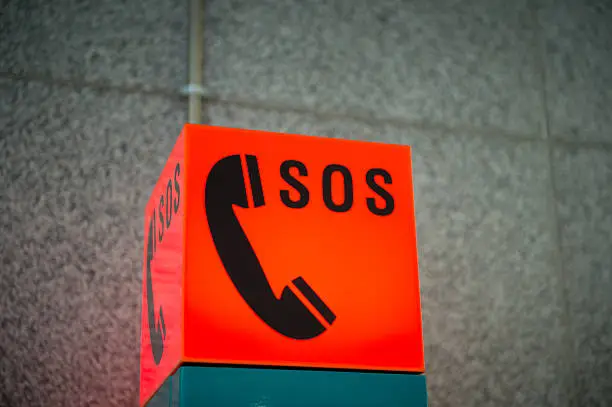 "An illuminated sign for an emergency phone, reading SOS and showing a phone, located at a train station."