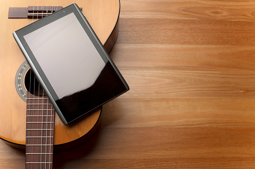 Acoustic guitar with digital tablet, wood background