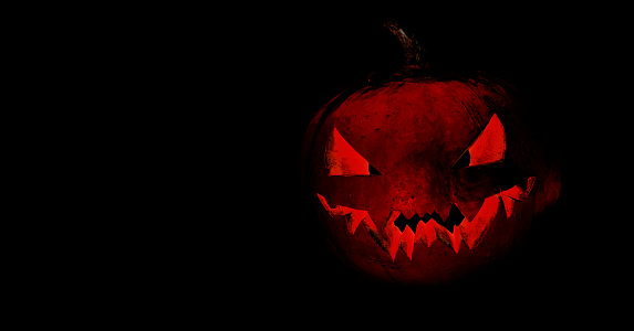 A scary image of a Halloween red pumpkin on a black background. Creepy face carved into a pumpkin. Monster. Happy Halloween