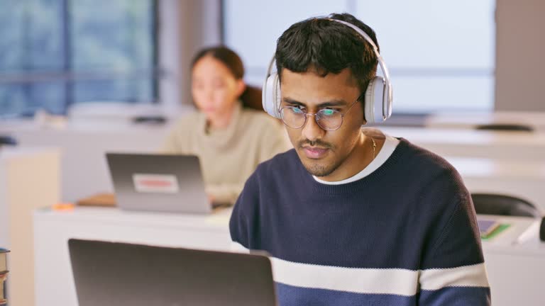 Headphones, computer and man study in the class listening to music, playlist or album at university. Technology, laptop and male student working on an assignment streaming a song or radio in college.