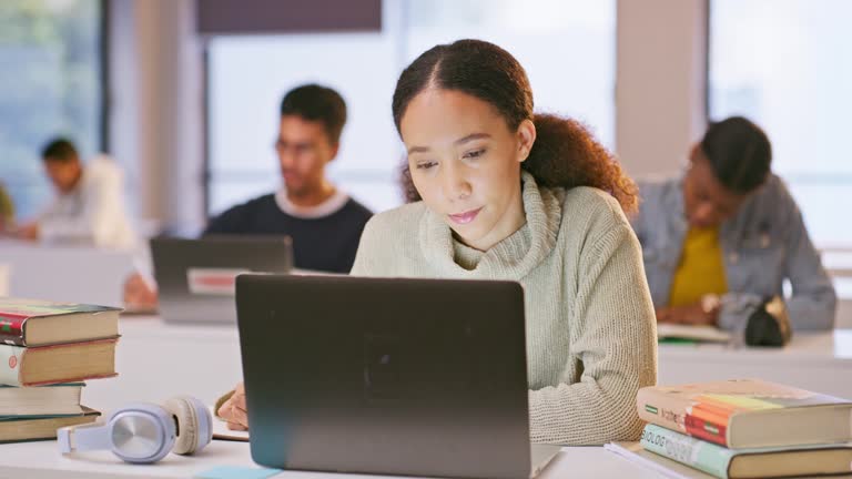 Woman, students and computer in classroom for writing notes, learning and research, planning or books for essay. African person typing on laptop at college, university or school for online studying