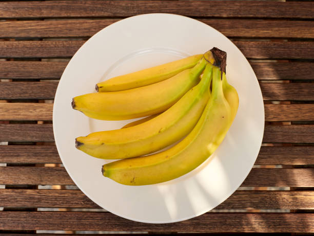 istock Fresh bananas on a white plate over wooden garden table. Top view. 1754162555
