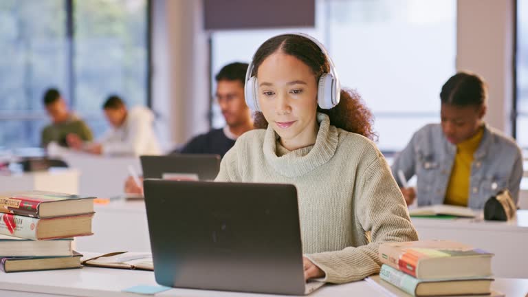 Headphones, computer and woman study in the class listening to music, playlist or album at university. Technology, laptop and female student working on assignment streaming song or radio in college.