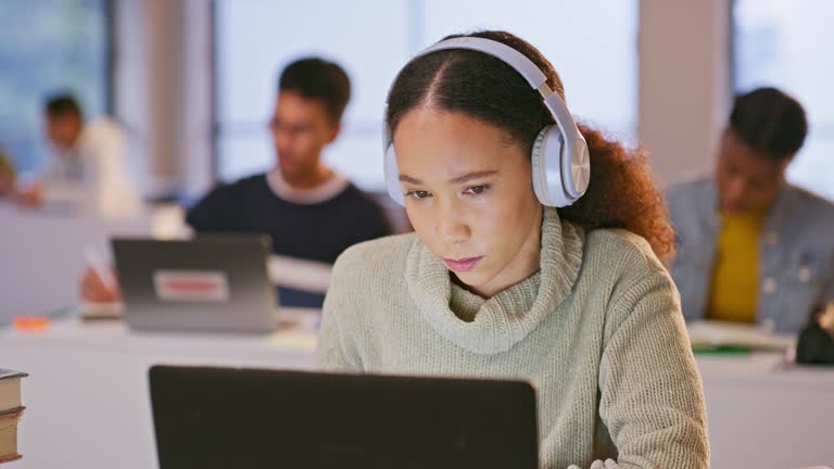 Headphones, computer and woman in the classroom listening to music, playlist or album at university. Technology, laptop and female student working on assignment streaming song or radio in college.