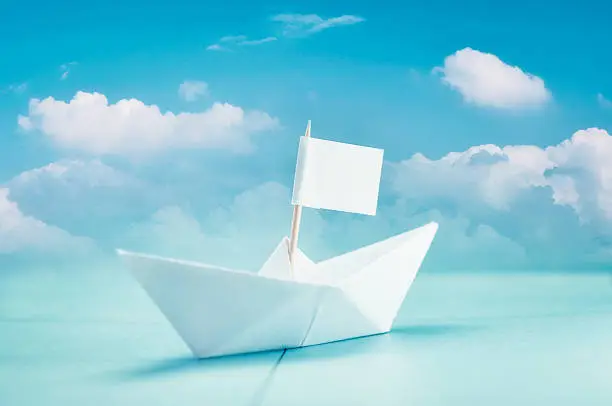 Paper boat standing on a map with a cloudy blue sky