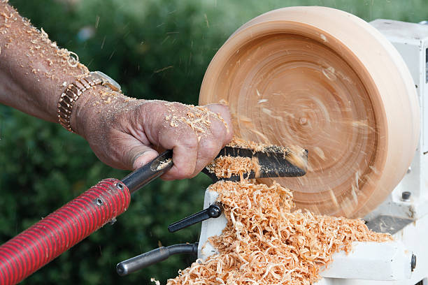 The hand of a woodworker using special tools to carve a wooden bowl spinning on a lathe.
