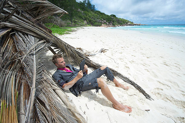 castaway homme d'affaires se détend avec tablette numérique à la plage - computer humor stranded business photos et images de collection