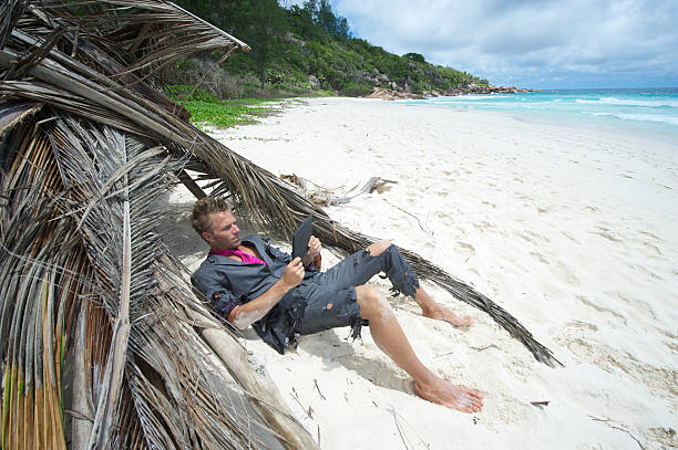 náufrago empresário relaxar com tablet digital na praia - computer humor stranded business imagens e fotografias de stock