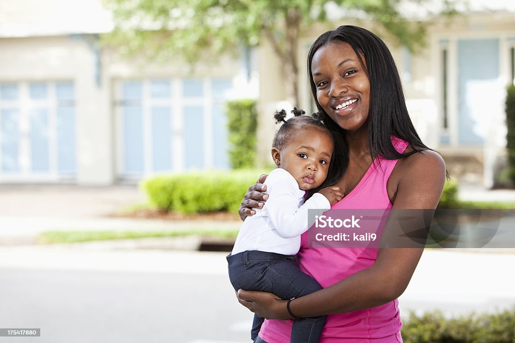 African American mother holding baby in front yard African American mother (20s) holding baby (8-9 months) in front yard. Baby - Human Age Stock Photo