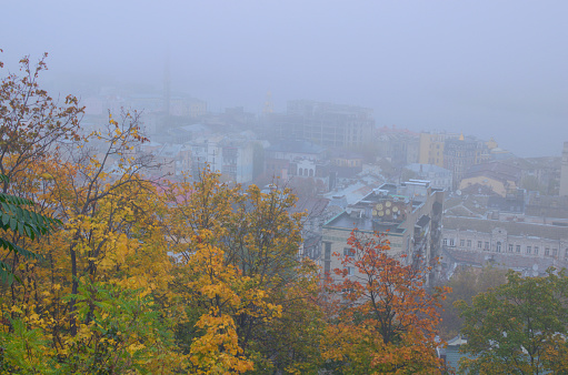 Aerial foggy landscape view of ancient Podil neighborhood. Mysterious cityscape. Kyiv in autumn thick fog. Tree leaves boarder.