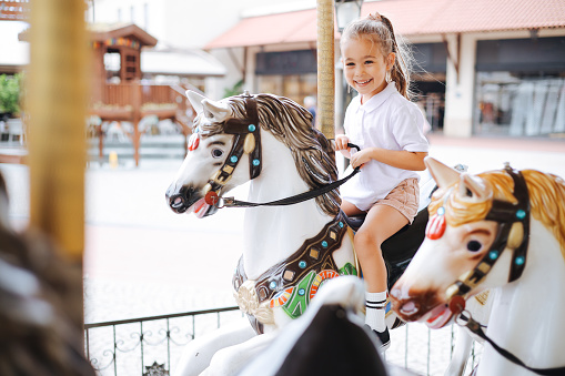 Pretty kid on carousel horse. Cute girl is riding attraction. Fun celebration