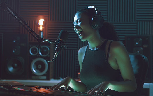 Young female artist recording a song in the studio, she is singing and playing the keyboard