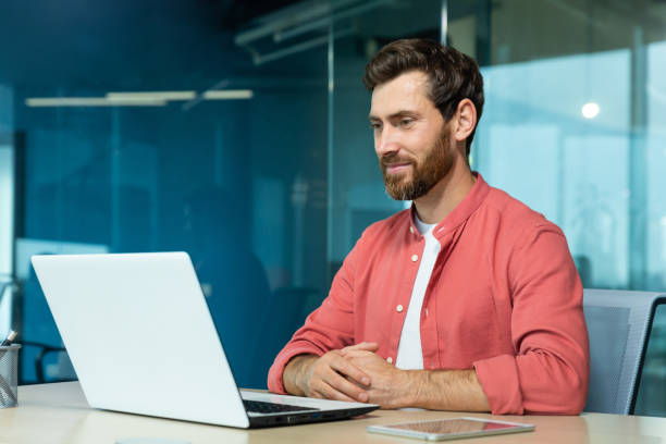 istock Mature adult businessman working on laptop inside office, programmer smiling contentedly reading and checking software code, man in red shirt 1754201038