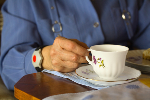 Senior woman's hand with coffe cup and emergency bracelet. Old almost 100 year old woman sitting at table and having a coffee break. Bracelet is for sos calling in any case of falling or illness.