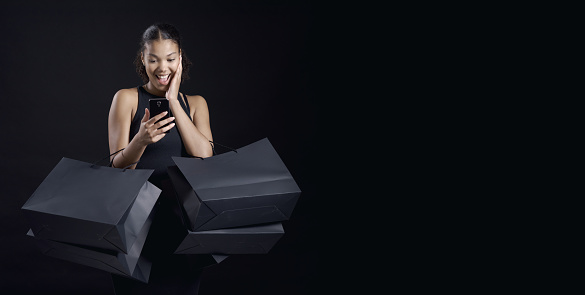 Beautiful young woman holding black shopping bags and a smartphone: Black Friday sale concept