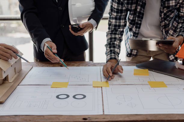 istock Three construction workers sit and discuss construction plans. A team of foremen and engineers talk with blueprints at the house construction site to check the house plans before starting work. 1754207248