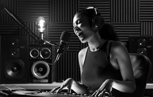Young female artist recording a song in the studio, she is singing and playing the keyboard
