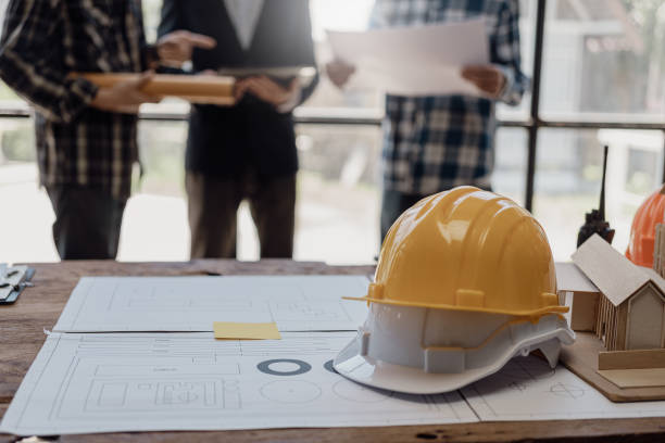 istock Three construction workers sit and discuss construction plans. A team of foremen and engineers talk with blueprints at the house construction site to check the house plans before starting work. 1754207256