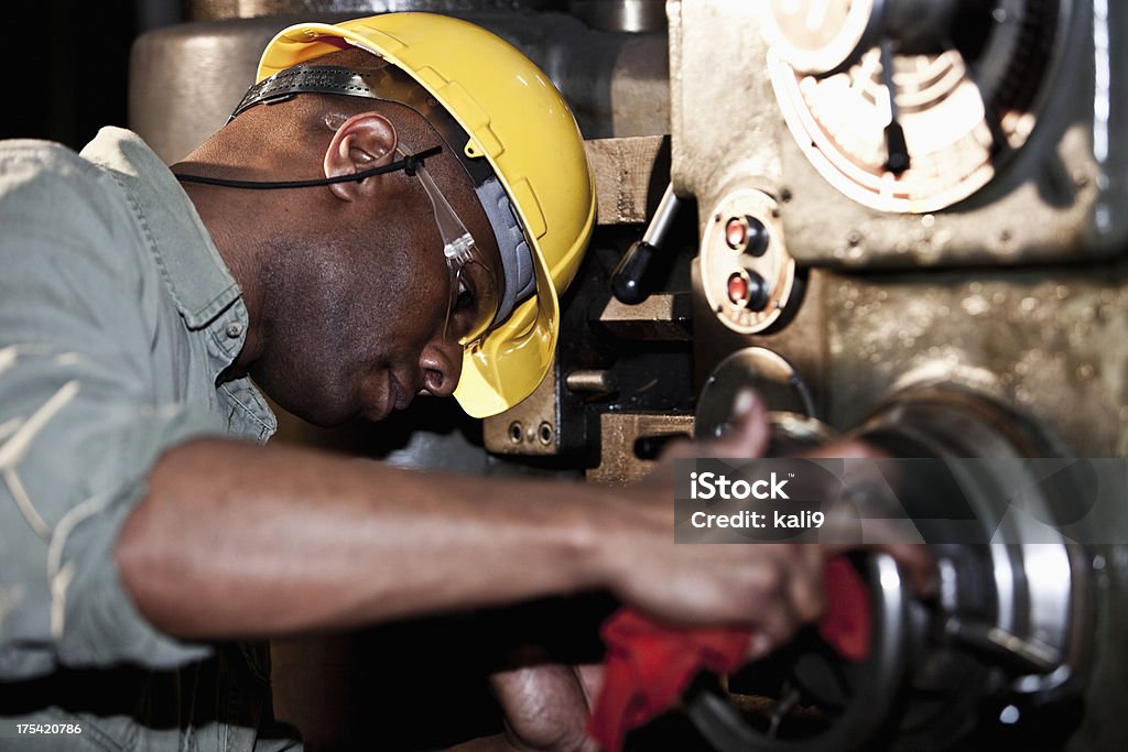 African American worker using drill press African American worker (30s) in fabrication shop using drill press. Machinery Stock Photo