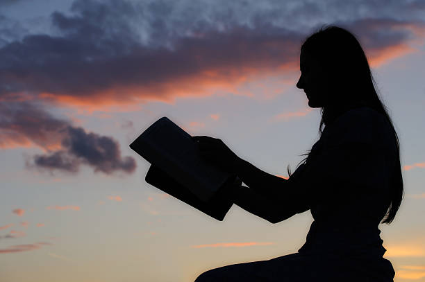 Silhouette of a young girl reading from bible.