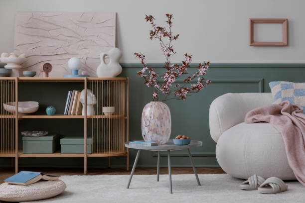 istock Spring composition of living room interior with mock up poster frame, boucle sofa, round coffee table, glass vase with flowering branches, beige carpet and personal accessories. Home decor. Template. 1754215816