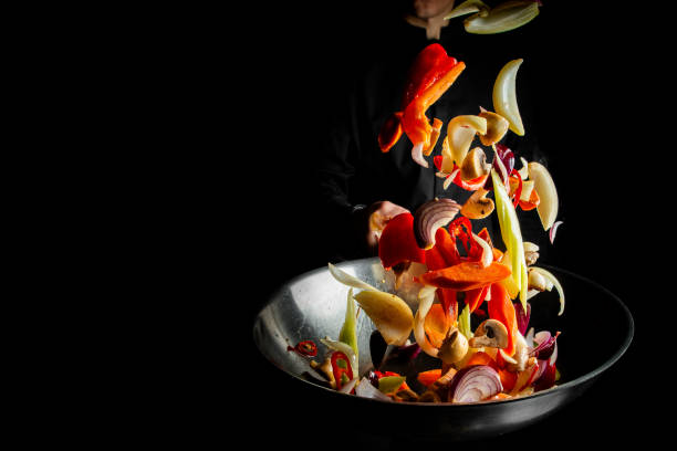 istock Closeup of chef throwing vegetable mix from wok pan on black background. 1754220326