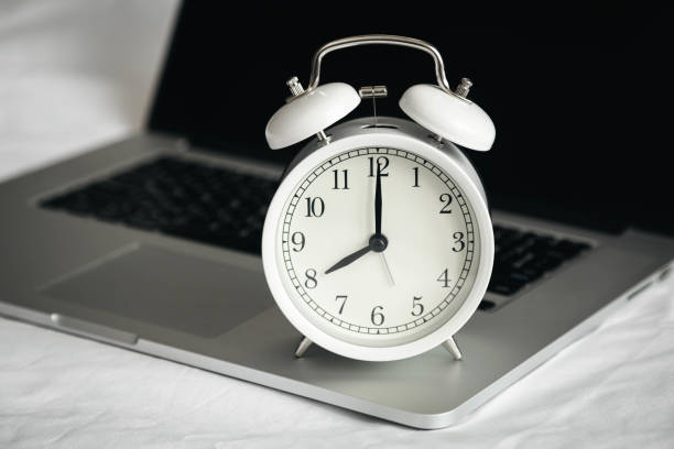 istock White alarm clock and laptop in a white bed, close up. 1754220336