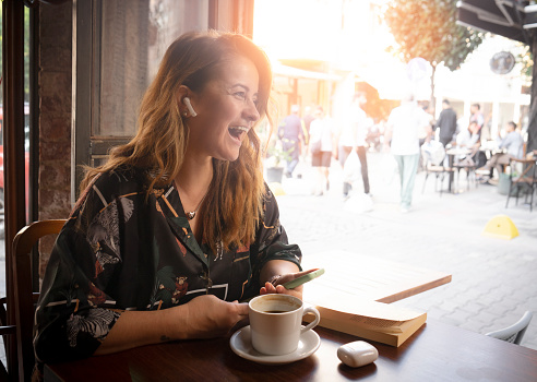 Happy young woman using mobile phone and enjoying coffee at cafe