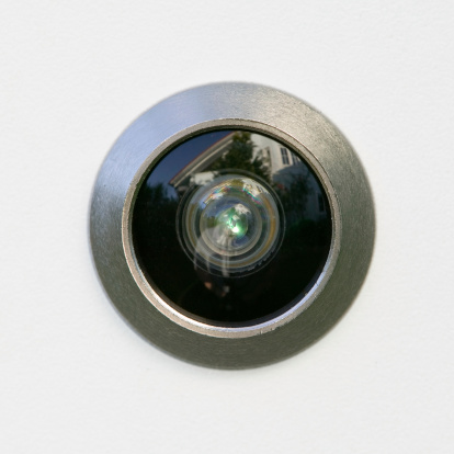 Closeup of a chrome peephole on white background/door