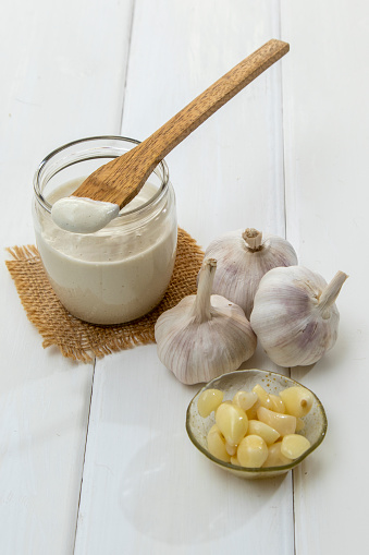 Bowl of Garlic sauce, garlic bulbs, spoon, on white counter