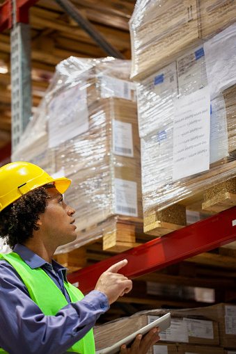 Mid-shot low angle view of young African American storage packer checking package inventory inside industrial warehouse facility