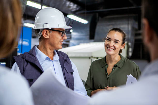 Warehouse supervisor discussing business matters with female manager while looking at blueprints