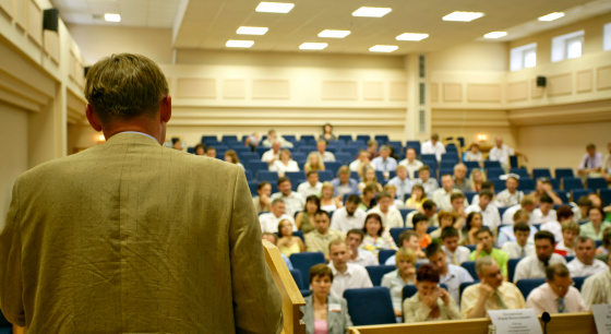 A man is making a speech in front of a big audience at a conference hall.
