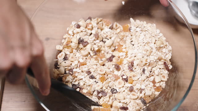 Ingredients for Granola, grains and a mixture of nuts and fruits, are being mixed together in a large bowl.