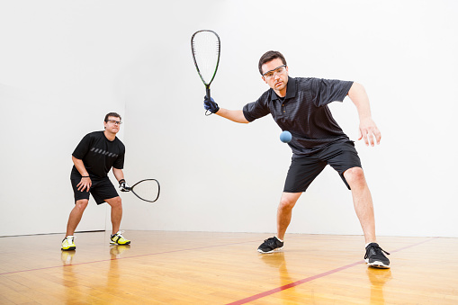 Two men playing racquetball on court. Shot at 1/100 of a second shutter speed to create a slight blurred motion to reveal the fast motion of racquetball.