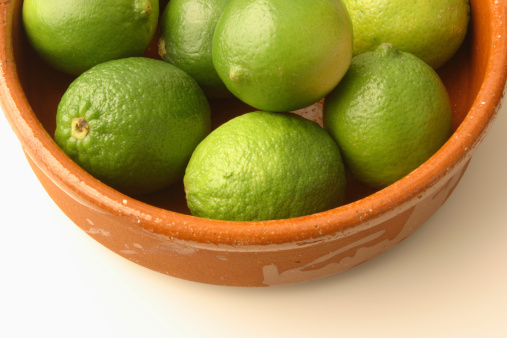 Subject: Green Persian Limes in a terr-cotta bowl on a white background