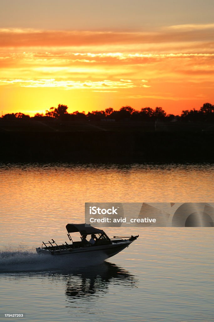 Boat on Water at Sunset A small fishing boat heads home after a great day of fishing as the setting sun paints the sky and the water a beautiful yellow orange. Back Lit Stock Photo